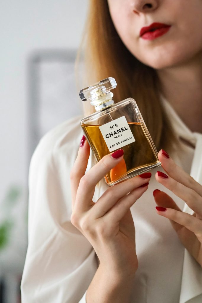 Close-up of a woman holding Chanel No. 5 perfume in a stylish indoor setting.