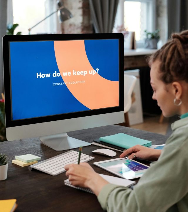 A woman at a desk using a computer and tablet in a modern home office.
